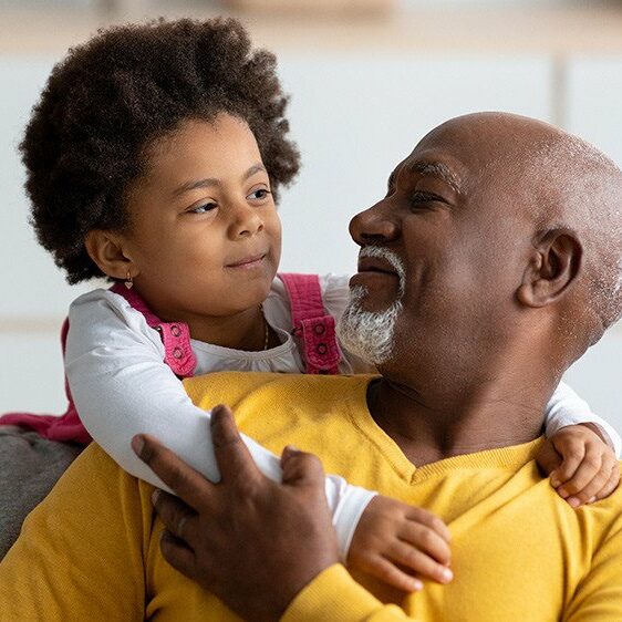 Cheerful little girl hugging grandfather from back